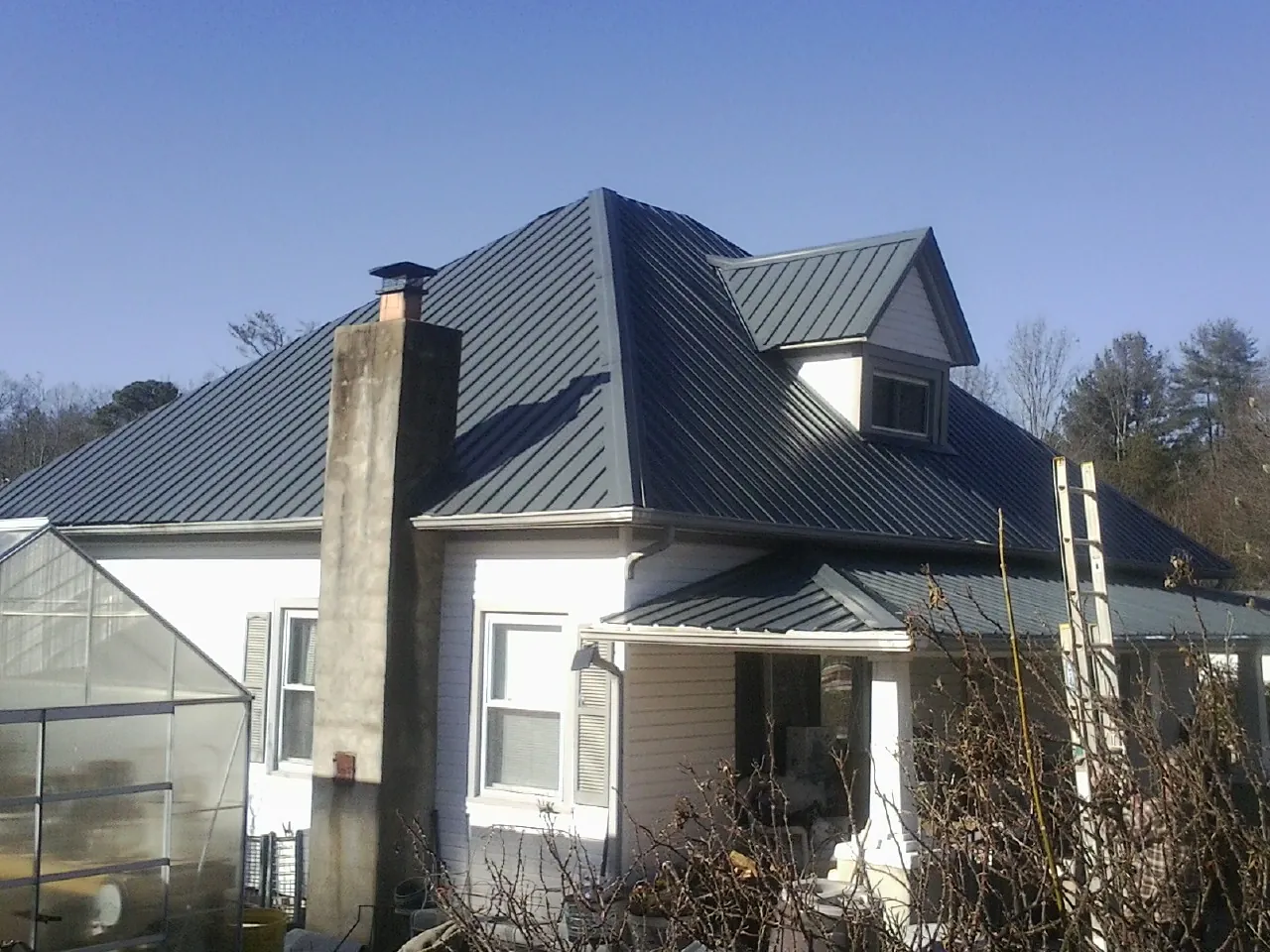 Dark blue standing seam metal roof on a white farmhouse with dormer — Slate & Tile Roof Repair by Roofing Brothers in Serena