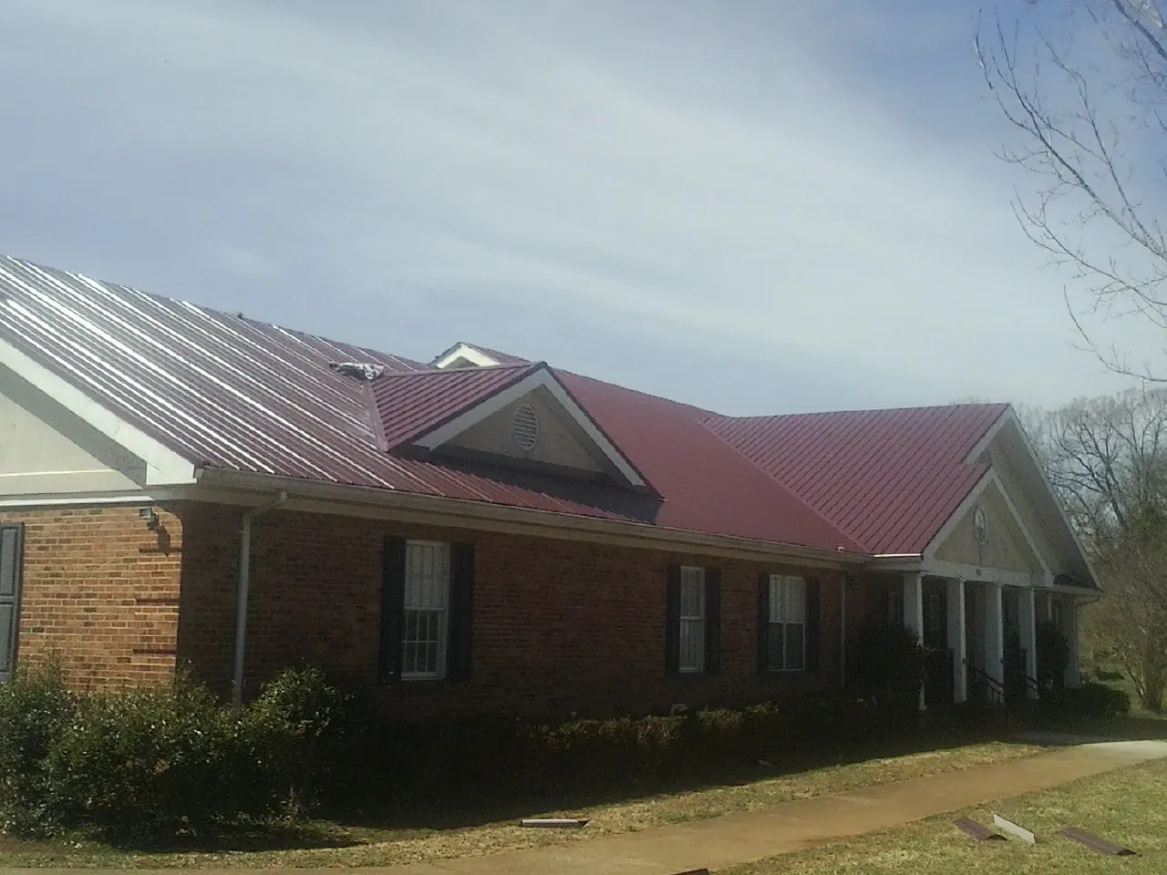 Red metal roof with gabled entries on a long brick building, from a Hail Damage Roof Repair job in Serena