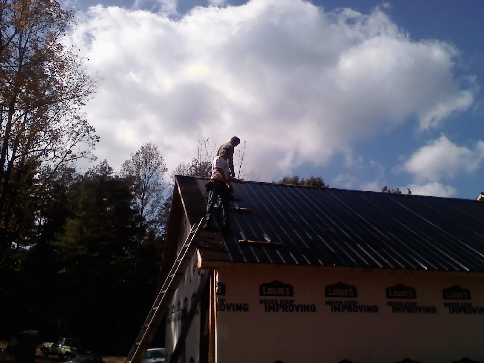Roofer fastening dark metal panels high against a cloudy sky, from a Roof Inspection job in Serena